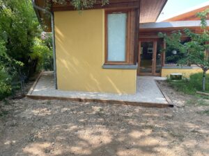 Bordure de gravier blanc longeant le mur jaune d'une maison moderne avec finitions en bois et jardin.