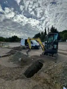 Mini-pelle Miravet TP creusant une tranchée sur un chantier avec un fourgon utilitaire G3R en arrière-plan.