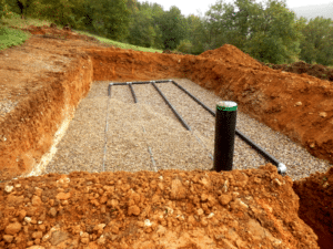 Installation d'un système d'assainissement avec tuyaux de drainage et gravier dans une excavation de terre rouge.