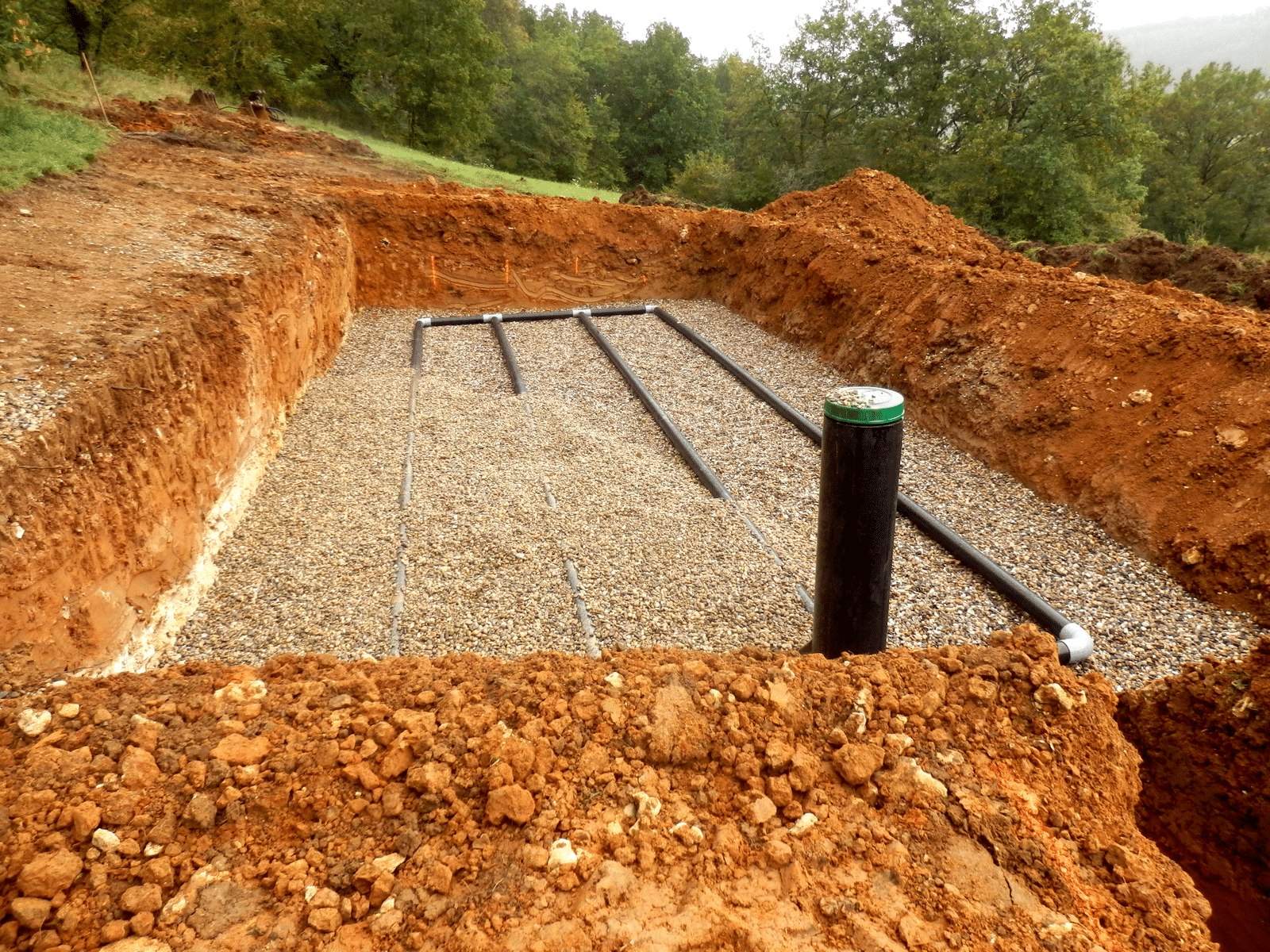 Installation d'un système d'assainissement avec tuyaux de drainage et gravier dans une excavation de terre rouge.