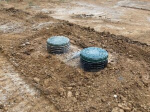 Deux couvercles de fosse septique verts sur des rehausses noires dans un terrain en terre en cours de travaux.