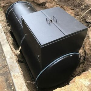 Cuve de stockage noire enterrée dans une tranchée avec trappe d'accès rectangulaire et poignée.