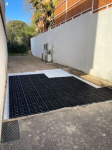Dalles de stabilisation noires sur feutre géotextile blanc pour l'aménagement d'une allée de jardin carrossable.