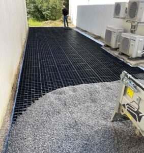 Gravier versé sur grilles de stabilisation noires dans une allée avec unités de climatisation Panasonic.
